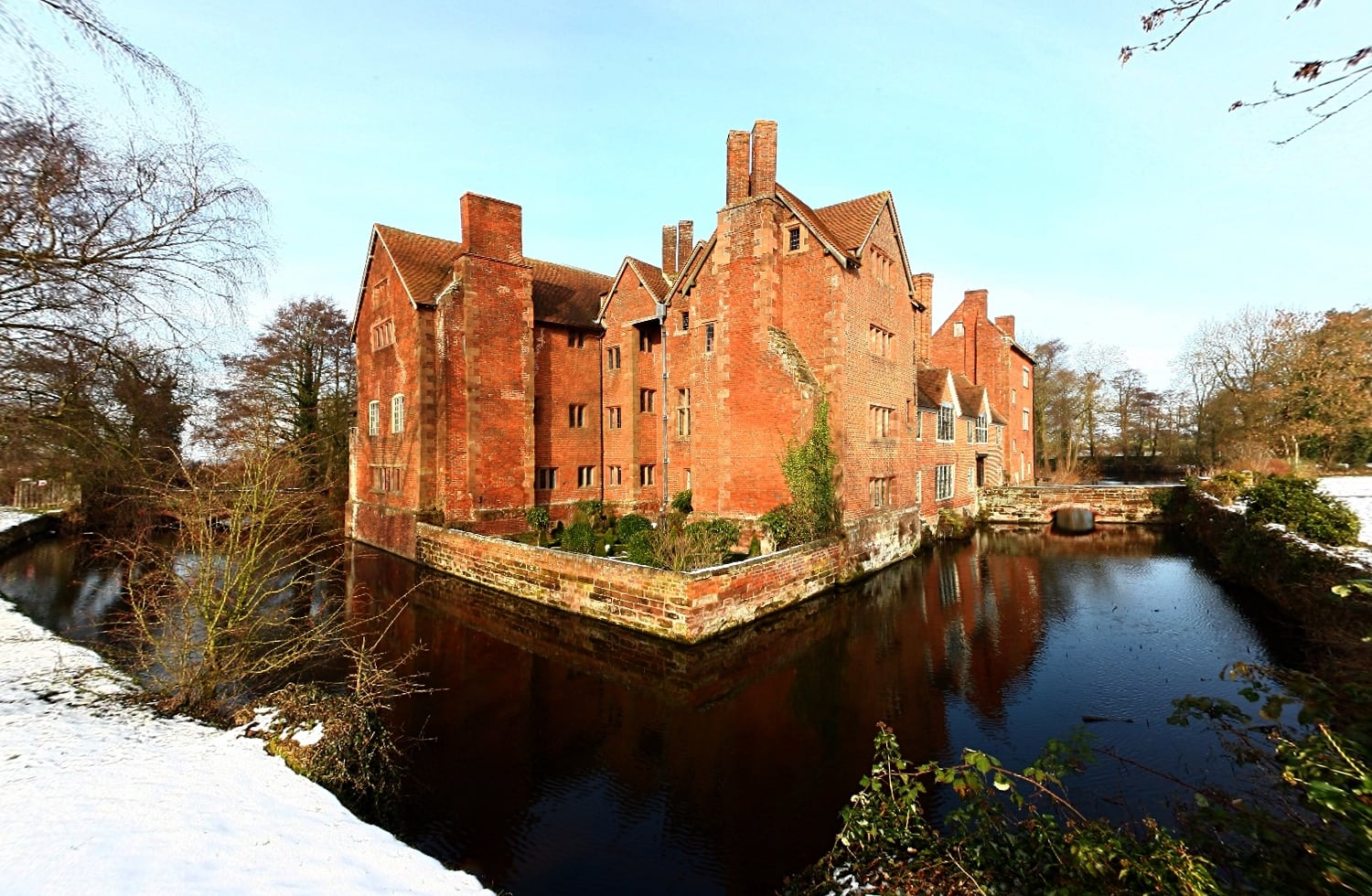 Harvington Hall, a red-brick Elizabethan house, seen across its moat in winter.